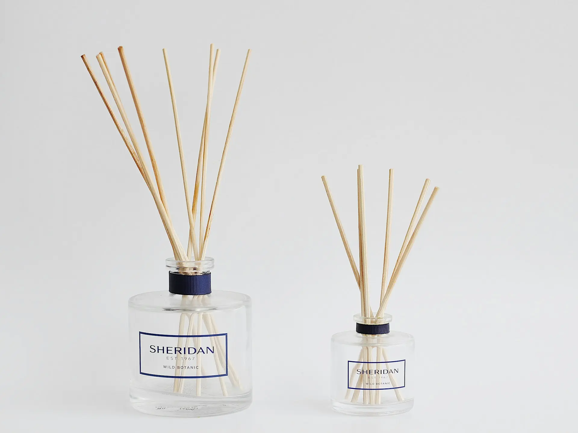 two bottles with reeds in them on a white surface
